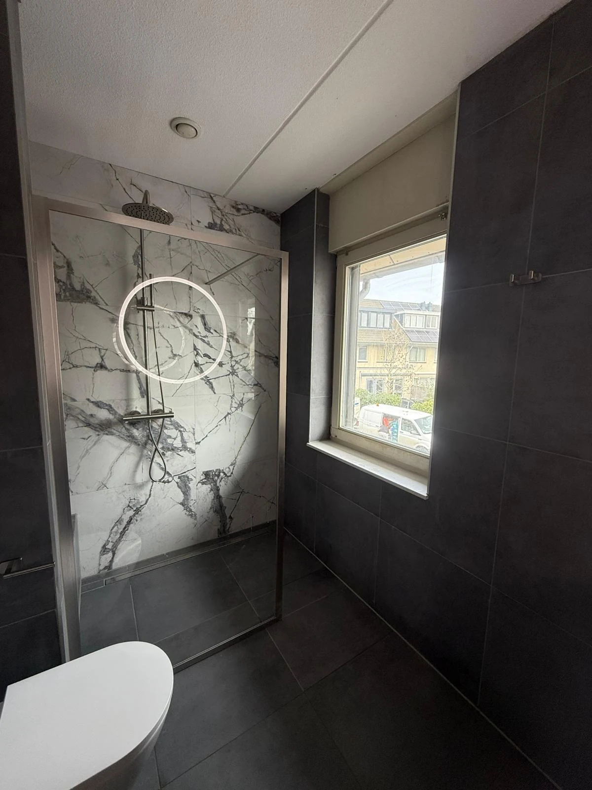 Douche met donkere tegels en een witte marmerlook achterwand