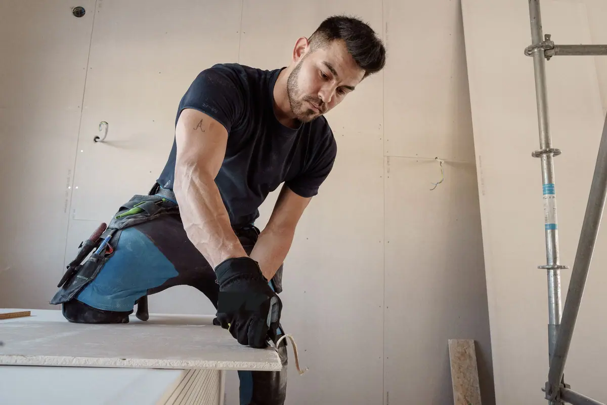 Vakman snijdt een gipsplaat op maat tijdens een verbouwing